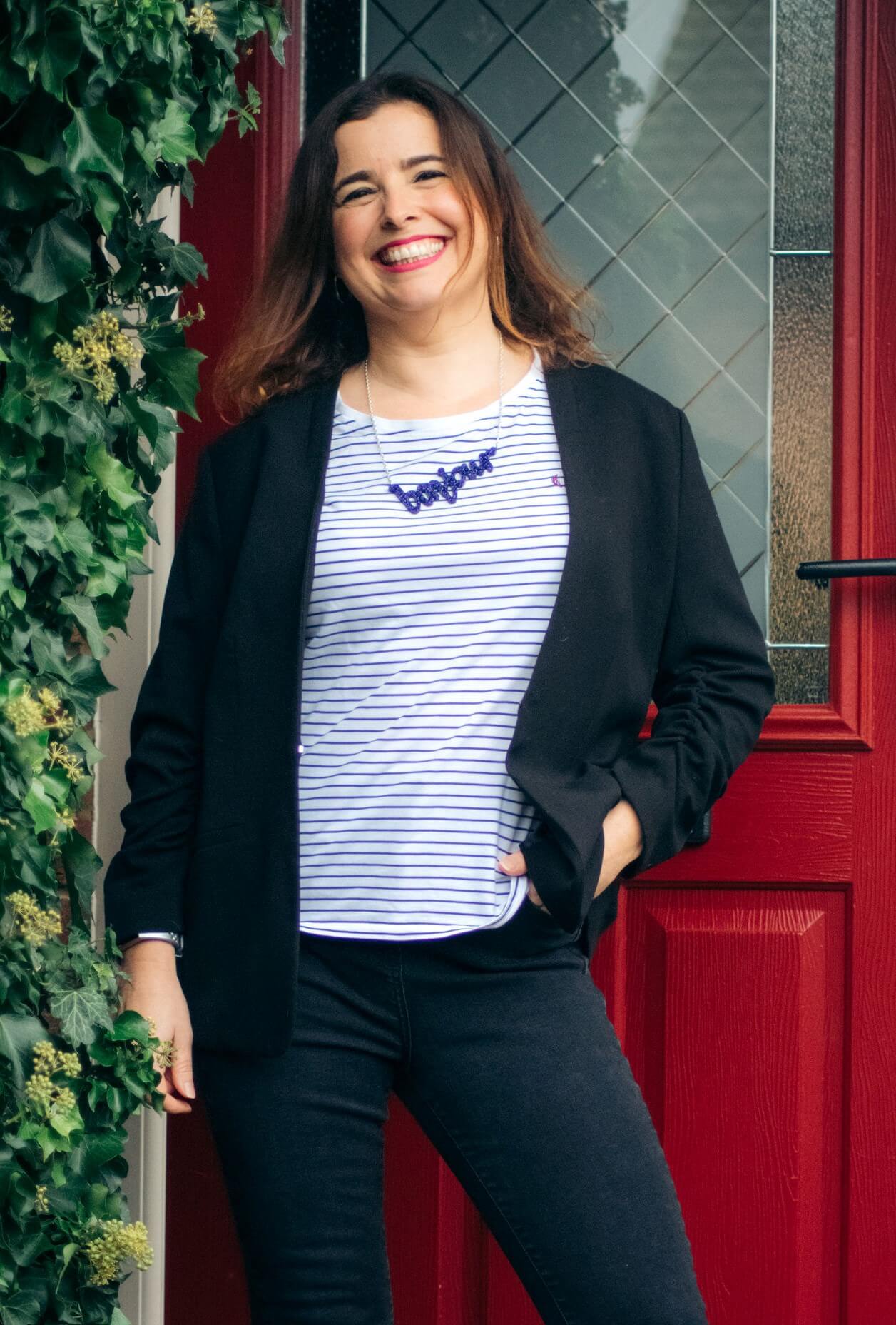 Frannie from Sound More French wearing a necklace saying Bonjour in front of a red front door