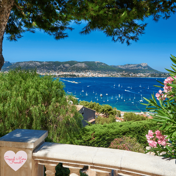 A breathtaking view of sailboats on the Mediterranean Sea, seen from a shaded balcony surrounded by lush greenery.