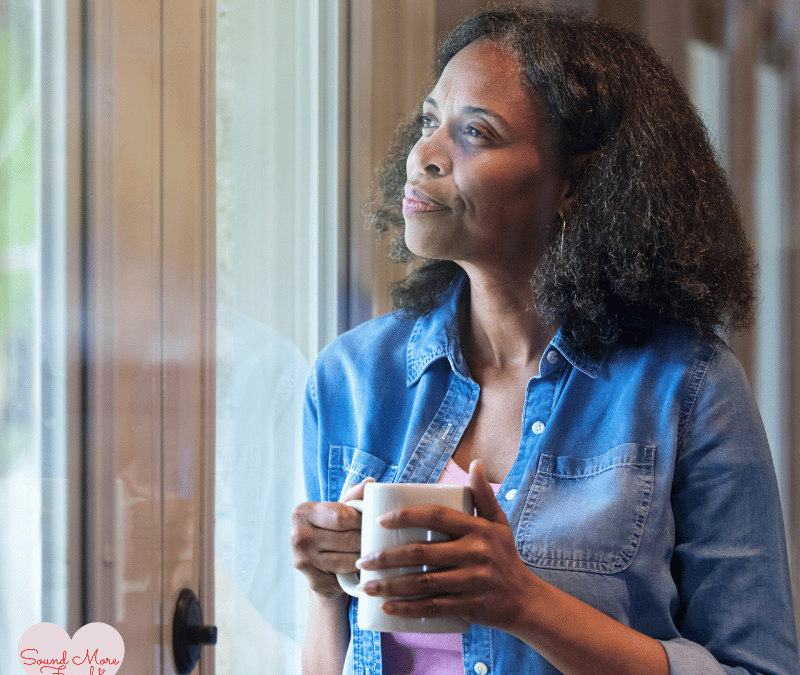 Woman wearing a denim shirt, holding a mug and gazing thoughtfully out of the window, dressed in bleu jean, reflecting a moment of calm or introspection.