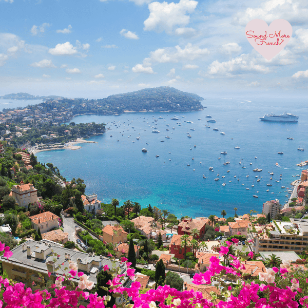 6 A vibrant view of the French Riviera, with colourful buildings, bright bougainvillaea, and boats dotting the sparkling blue bay.