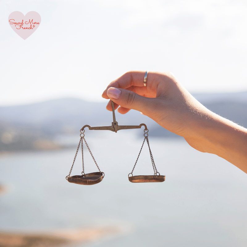 hand_holding_small_antique_balance_scales_outdoors_with_blurred_background_and_sound_more_french_logo