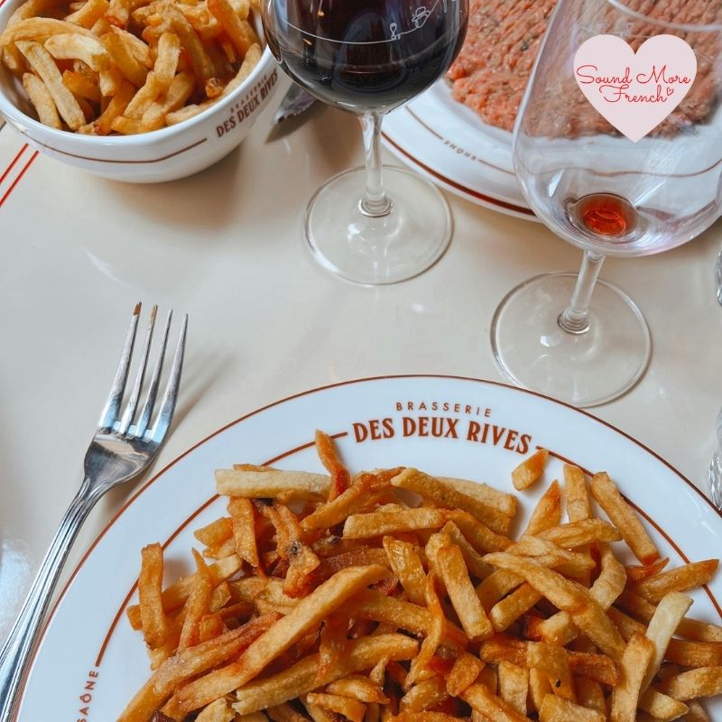 plate_of_french_fries_and_wine_glasses_on_brasserie_des_deux_rives_table_with_sound_more_french_logo