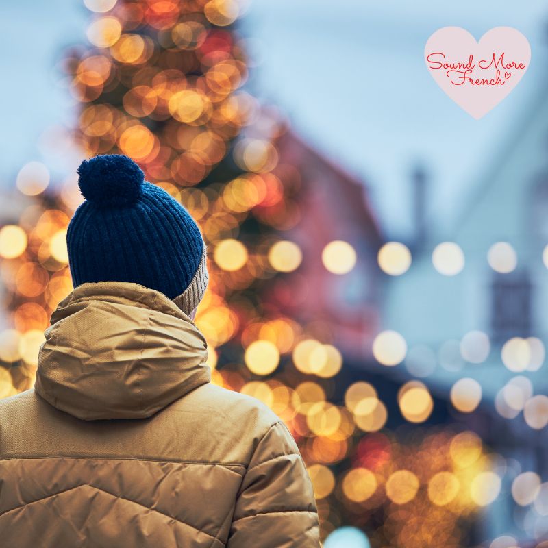 person_in_winter_coat_and_blue_hat_looking_at_christmas_tree_with_festive_bokeh_lights_with_sound_more_french_logo