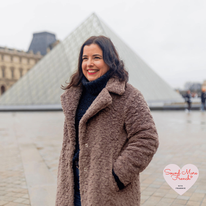 Frannie_smiling_near_the_Louvre_Pyramid_in_Paris_wearing_a_long_teddy_coat_and_dark_knit_jumper_on_a_grey_winter_day