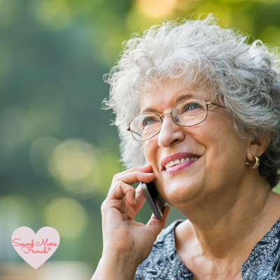 Older_woman_smiling_while_speaking_on_the_phone_outdoors_Sound_More_French_logo